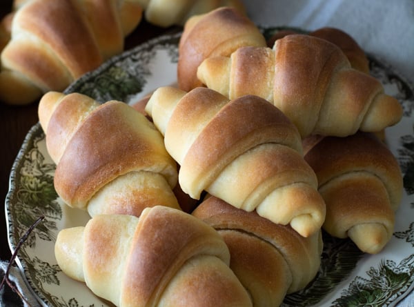 Baked crescent dinner rolls on a platter with linen cloth.